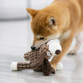 Dog playing with a plush toy on a light wooden floor.